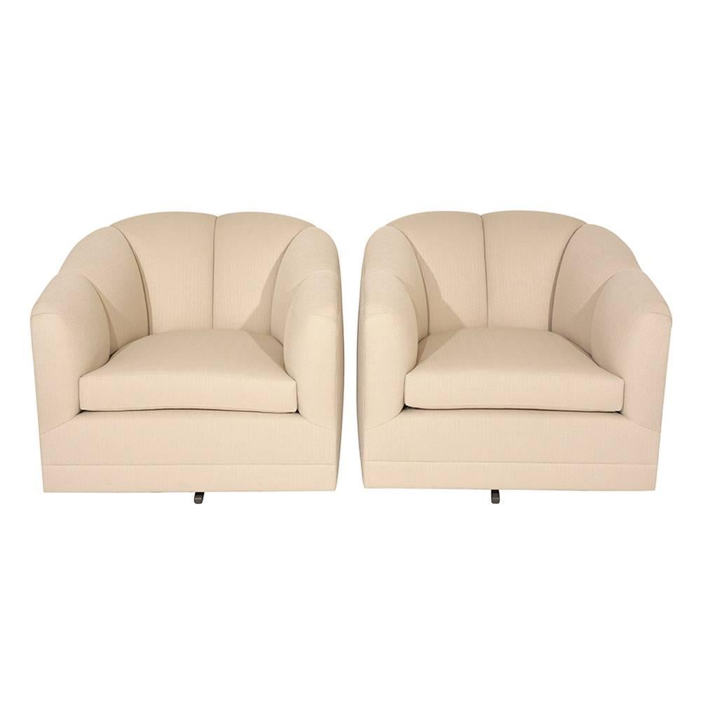 This pair of 1960s Mid-Century Modern-style swivel chairs are upholstered on all sides in a beige color fabric. The curved backs and arms feature a channel design that accents the profile of the chair. The seat is made from a comfortable new foam