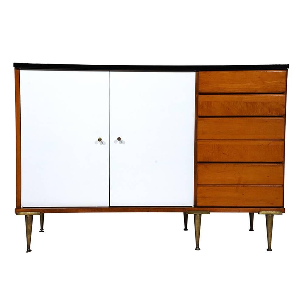 This 1960s Mid-Century Modern-style credenza is designed by Paul McCobb is made of wood finished in three colors: natural, white and black. The cabinet doors are finished in a stark white color with brass knobs. Inside there is a single wood shelf