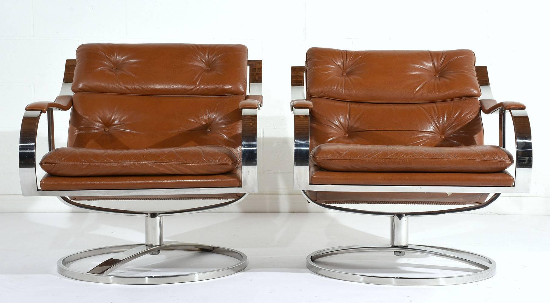 This pair of 1970s Mid-Century Moderns style swivel lounge chairs is made by Gardner Leaver. The steel frame is finished in chrome with rounded and square edges. The lounge chairs are upholstered in the original cognac colored leather in very good