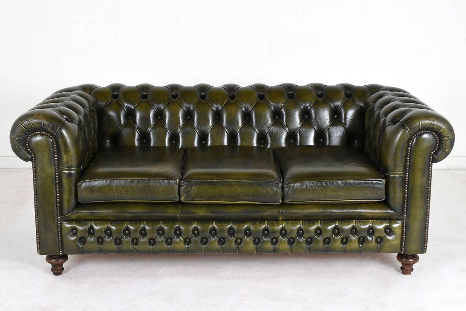 This 1950s, vintage Chesterfield-style sofa is upholstered in leather with the original green color dye and a beautiful patina. The scroll arms and back feature tufted and folded details. The arms are accented by brass nailhead decoration and the