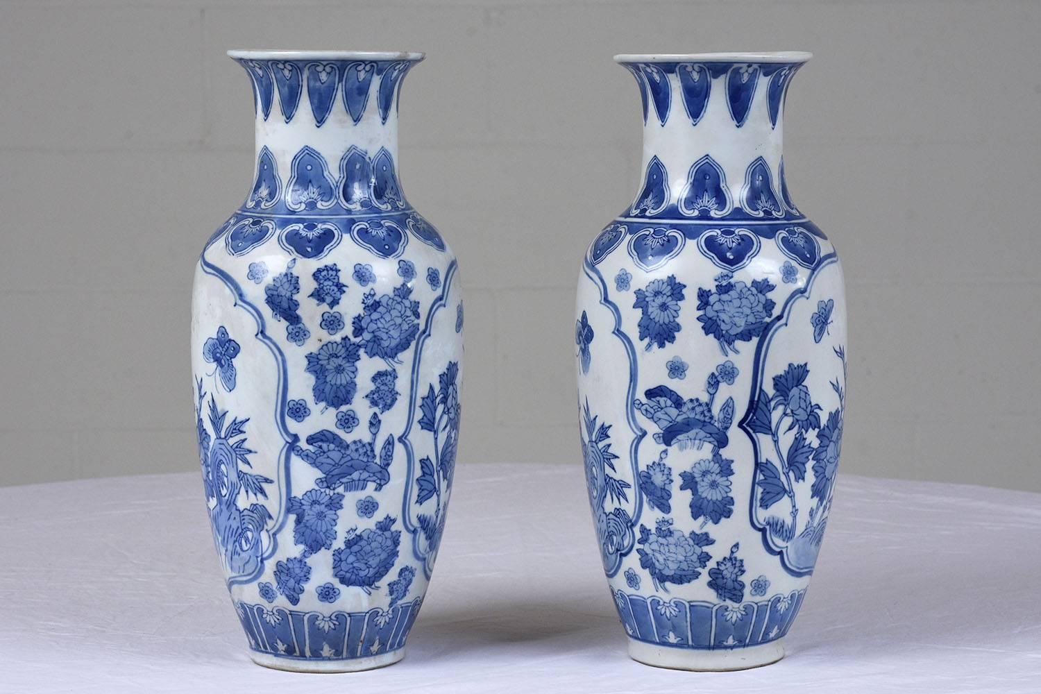This pair of 1910s Chinese vases are made of ceramic and feature blue and white designs. The vases depict a garden scene with butterflies flying. The vases have floral and leaf motif bands that adorn the lip and bottom. The vases are stamped on the