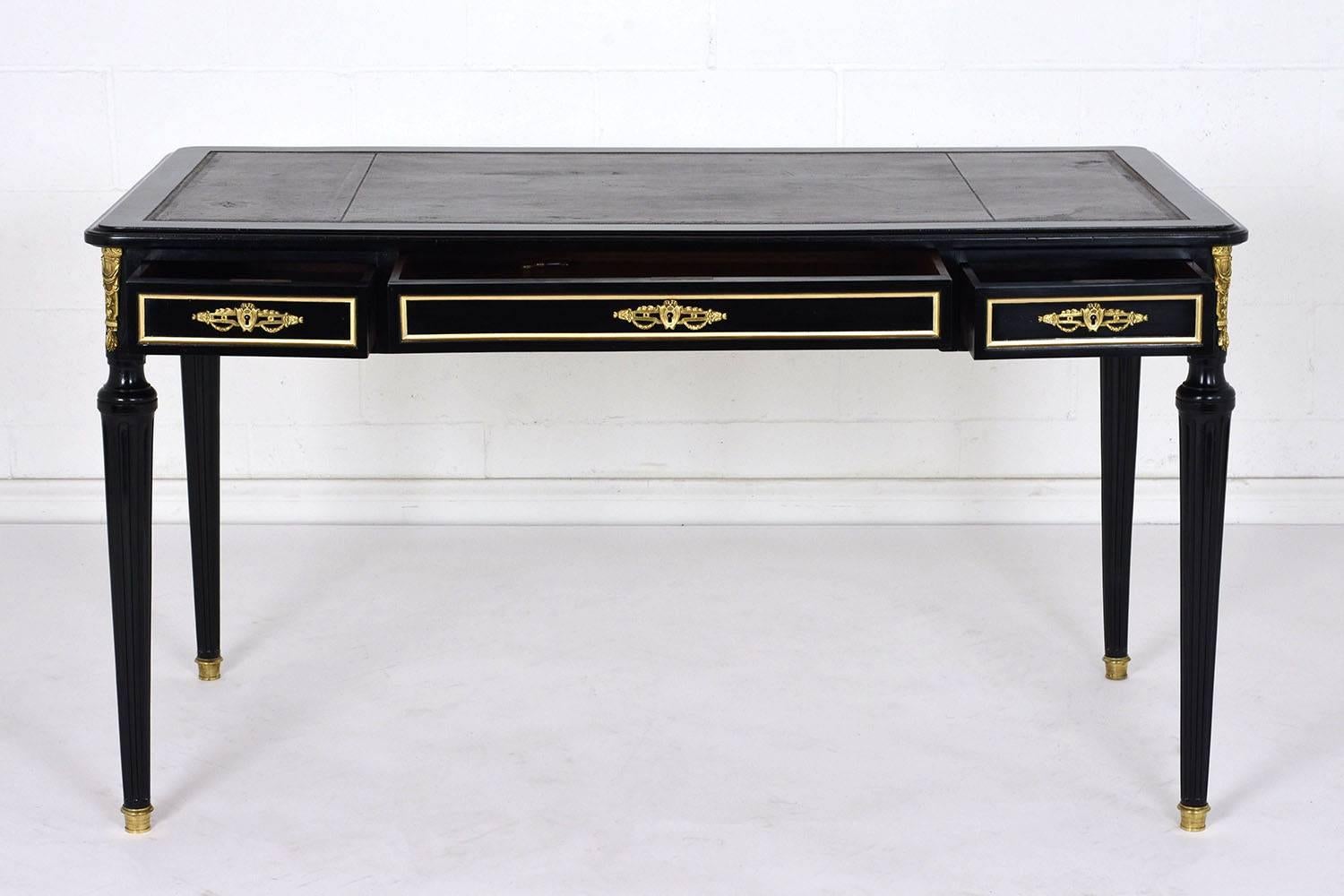 This 1900s French Louis XVI-style desk is made of mahogany wood that has been ebonized in a rich black color with a lacquered finish. The top of the desk features an embossed leather insert in a rich brown color. The front of the desk has three