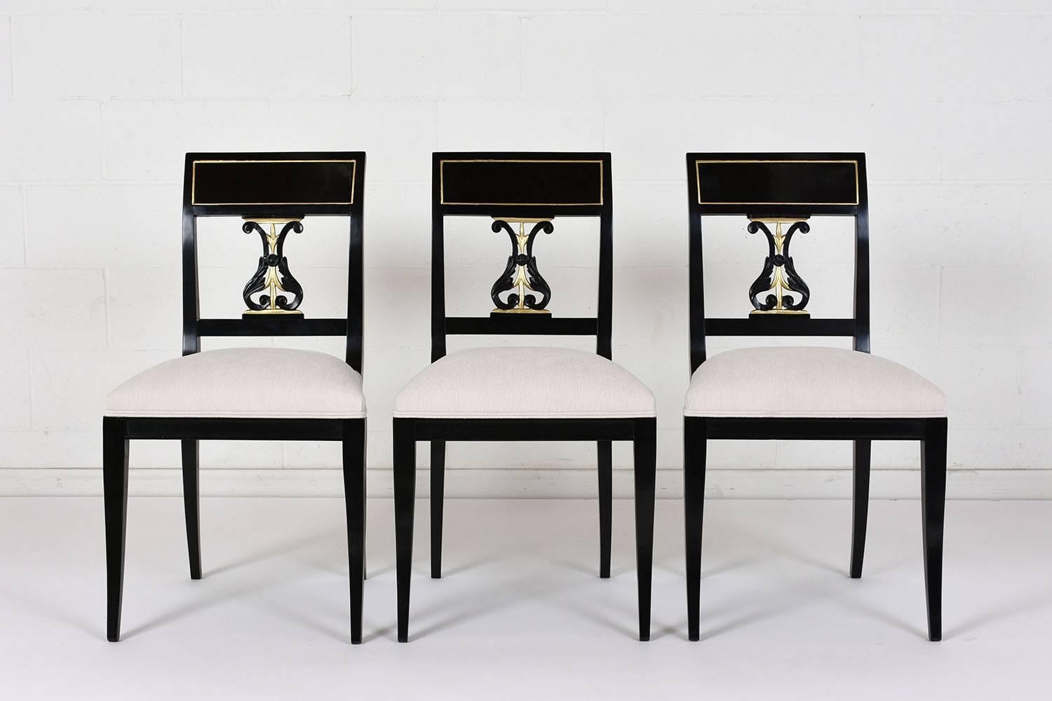 This set of eight 1930s Hollywood Regency-style dining chairs has two armchairs and six side chairs. The wood frames have been ebonized in a deep black color with a lacquered finish and gilt accents. The square seat backs have an intricate splat