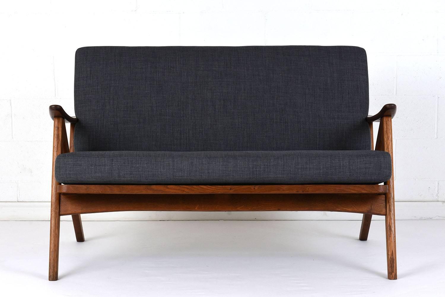This 1960s Danish Mid-Century Modern-style love seat is designed by Arne Hovmand Olsen. The teak wood frame is carved in a double V shape and features the original walnut stain with a lacquered finish. The frame features slats along the back and