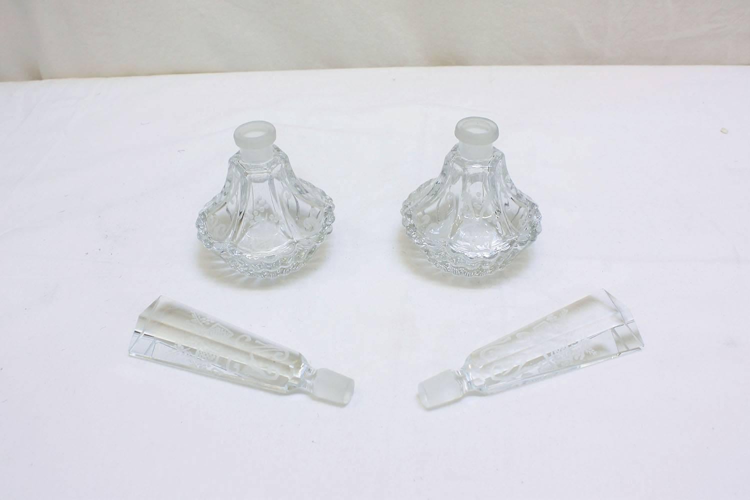 This pair of 1900s Baccarat perfume bottles are made of crystal. The faceted crystal features a scalloped edge and etched details. The handles and bottles are adorned with flowers, baskets, and scroll details. This pair of bottles are stunning and
