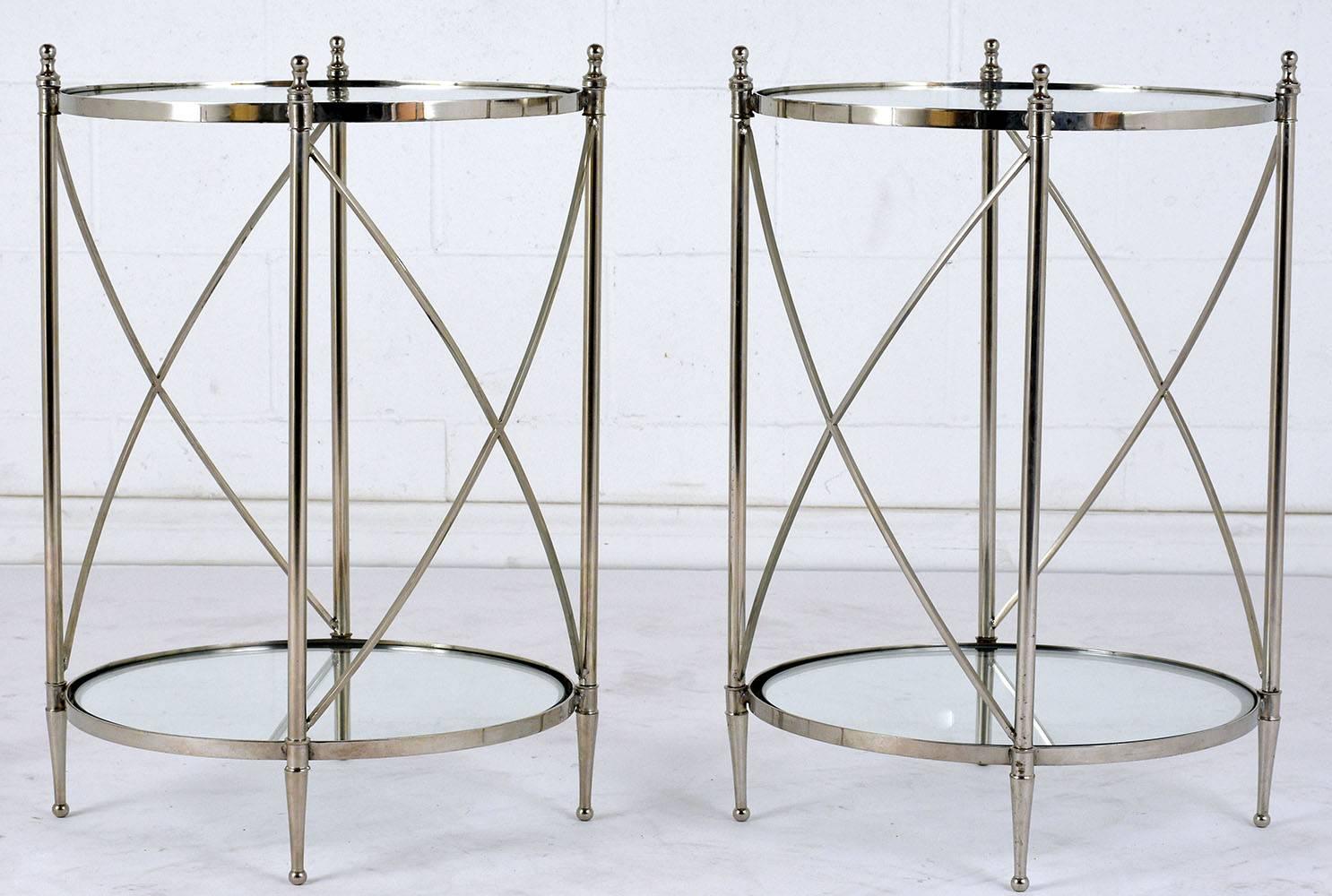 This pair of 1990s Regency-style side tables features a steel X-shaped frame with a chrome finish and is newly restored. The legs are accented by rounded finials at the top and tapered feet with ball bottoms. There is an open shelf at the bottom of