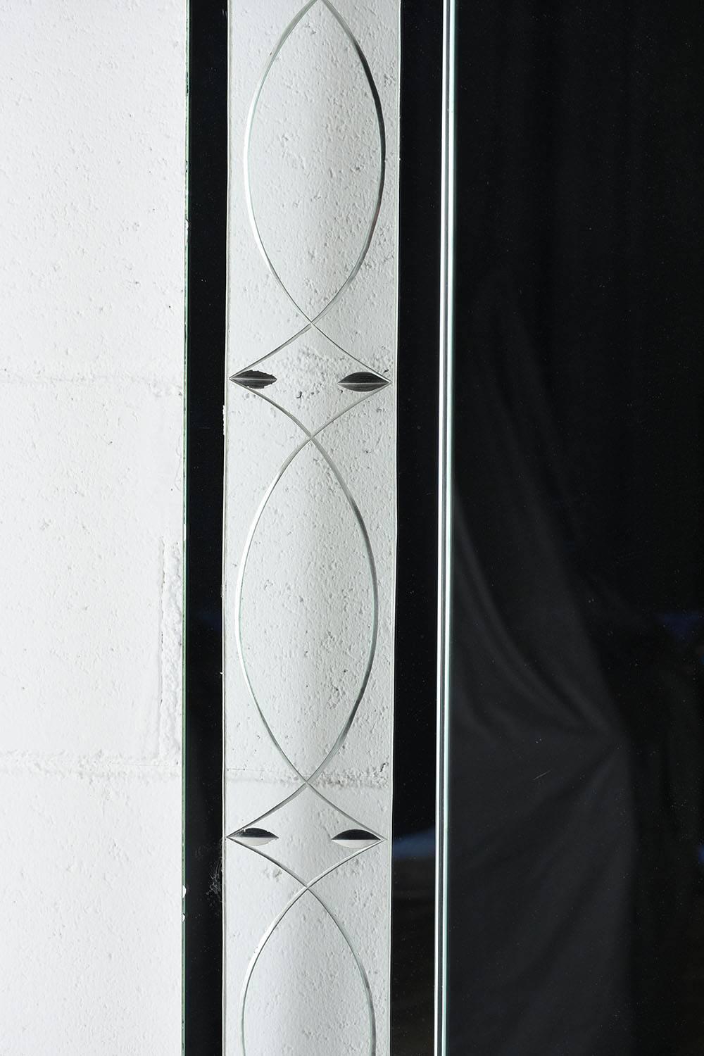 This 1960s Modern-style rectangular wall mirror features a glass and chrome frame. The frame has a chrome outer frame with raised corner accents and glass panel. The glass panels have decorative etches of diamonds and ovals. The main mirror is in