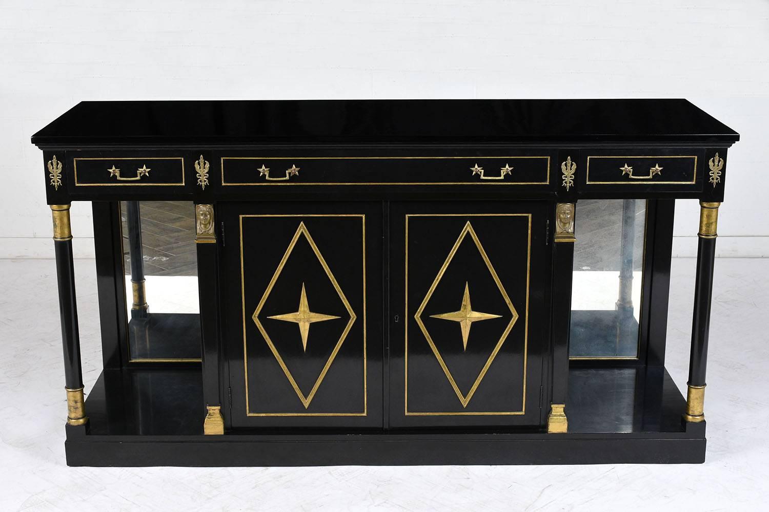 This 1950s Empire-style server or buffet is made of wood that has been ebonized with giltwood accents a lacquered finish. There are three drawers along the top with brass moulding details and decorative brass drawer pulls. In the centre below there
