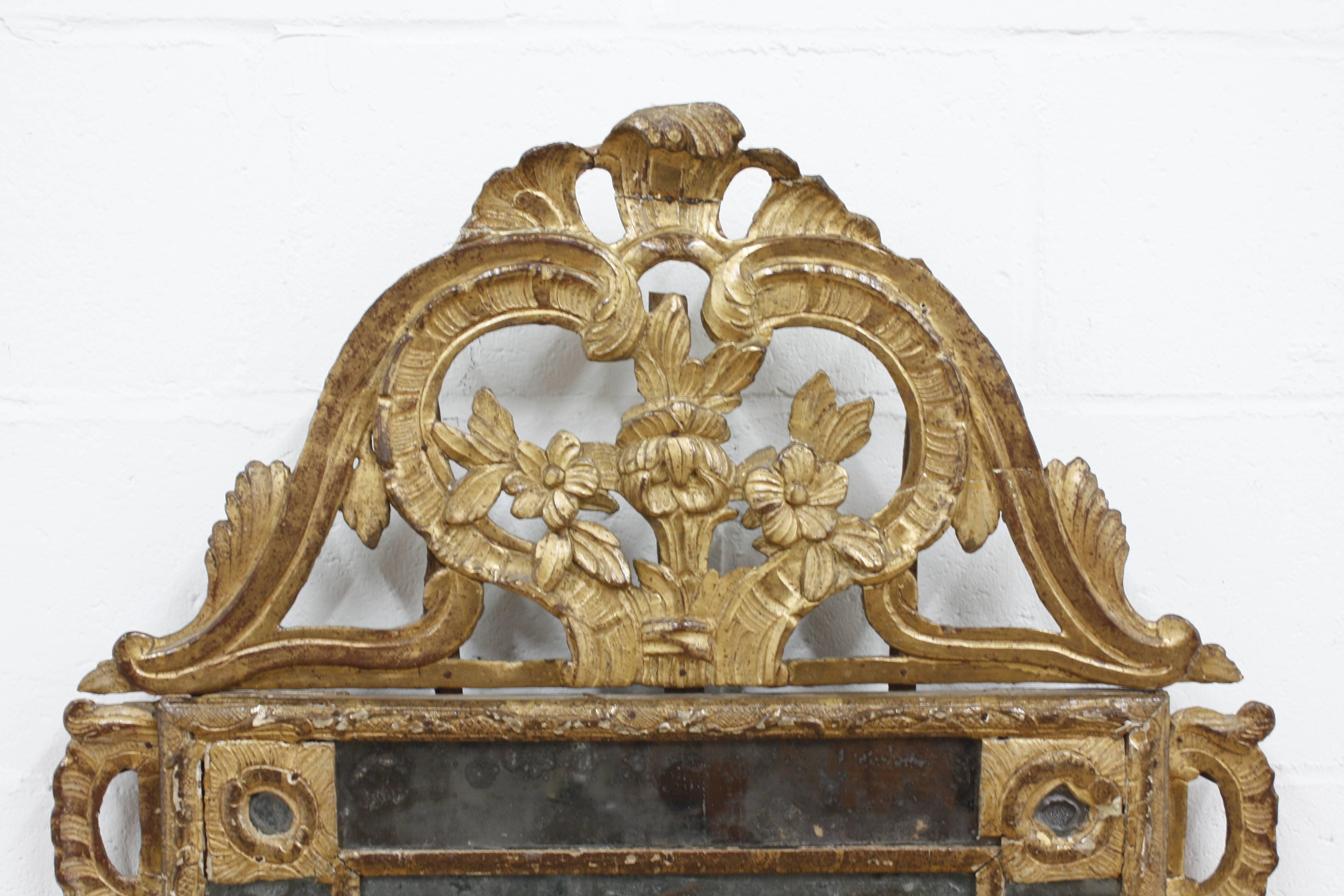 This 1790s French Louis XVI-style wall mirror features the original giltwood frame with ornate carvings. The frame features ornate carvings of flowers, acanthus leaves, ribbons, and decorative patterns. The original mirror is in fair condition with