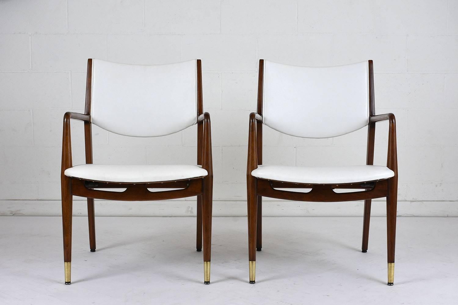 This pair of 1960s Mid-Century Modern style lounge chairs features a walnut wood frame that has been stained a rich walnut color with a lacquered finish. The frame has a classic frame with a decorative front edge and tapered legs. The font legs have