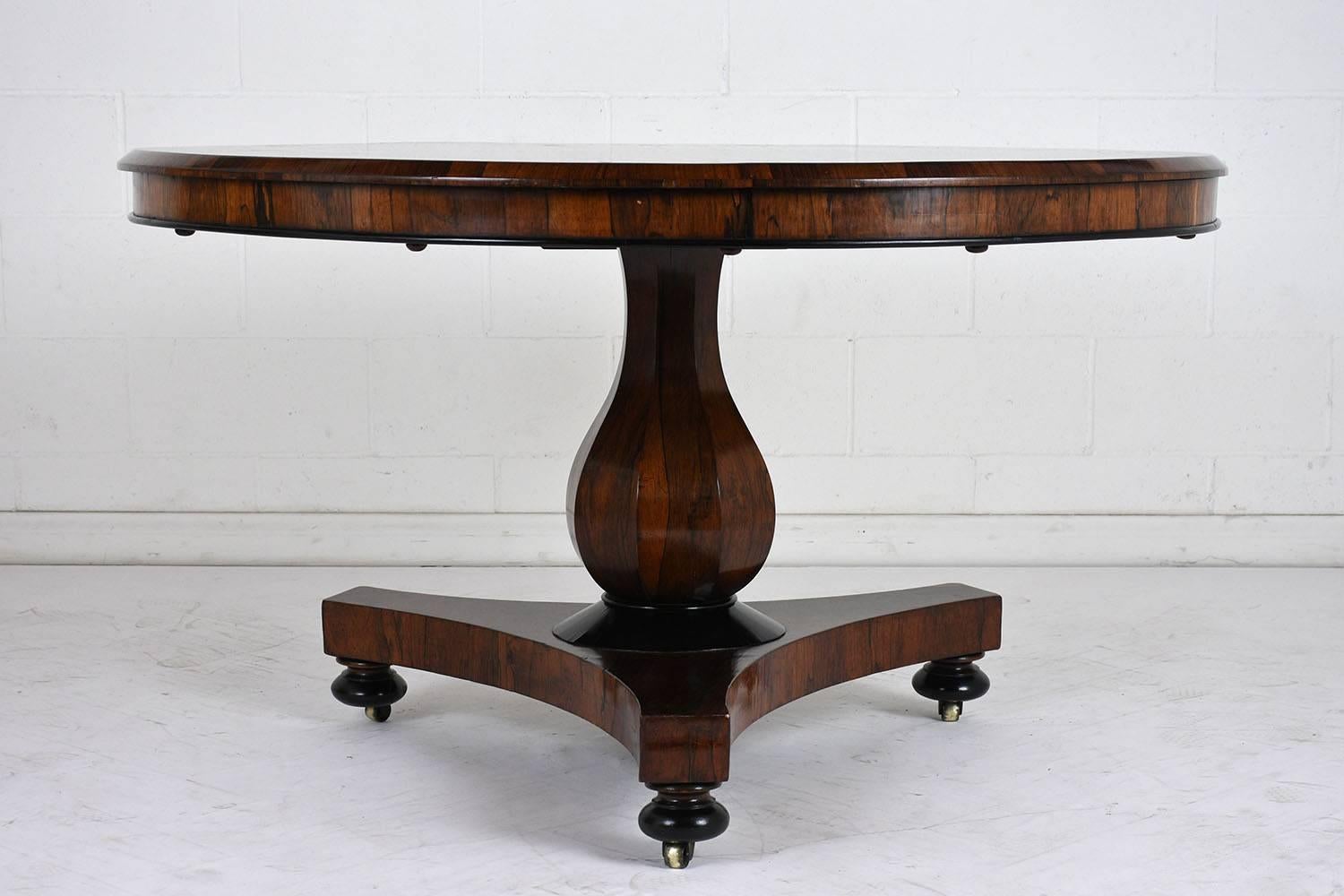 This 1860s French Empire-style center or dining table is made of rosewood stained in a rich rosewood color with a lacquered finish. The table has a beautiful natural patina with black accents on the edge, pedestal, and feet. The tabletop has a