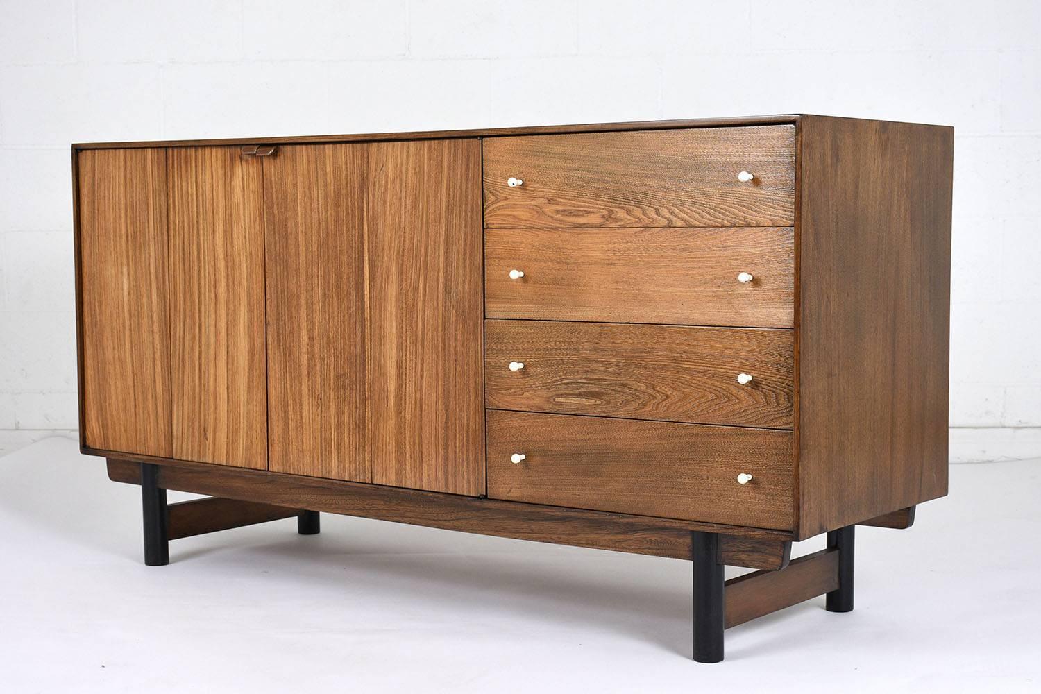 This 1960s Mid-Century Modern Credenza is made of walnut wood stained a walnut color with a polished finish and has been fully restored. This buffet features four drawers with white rubber coated drawer pulls, two accordion cabinet doors that close