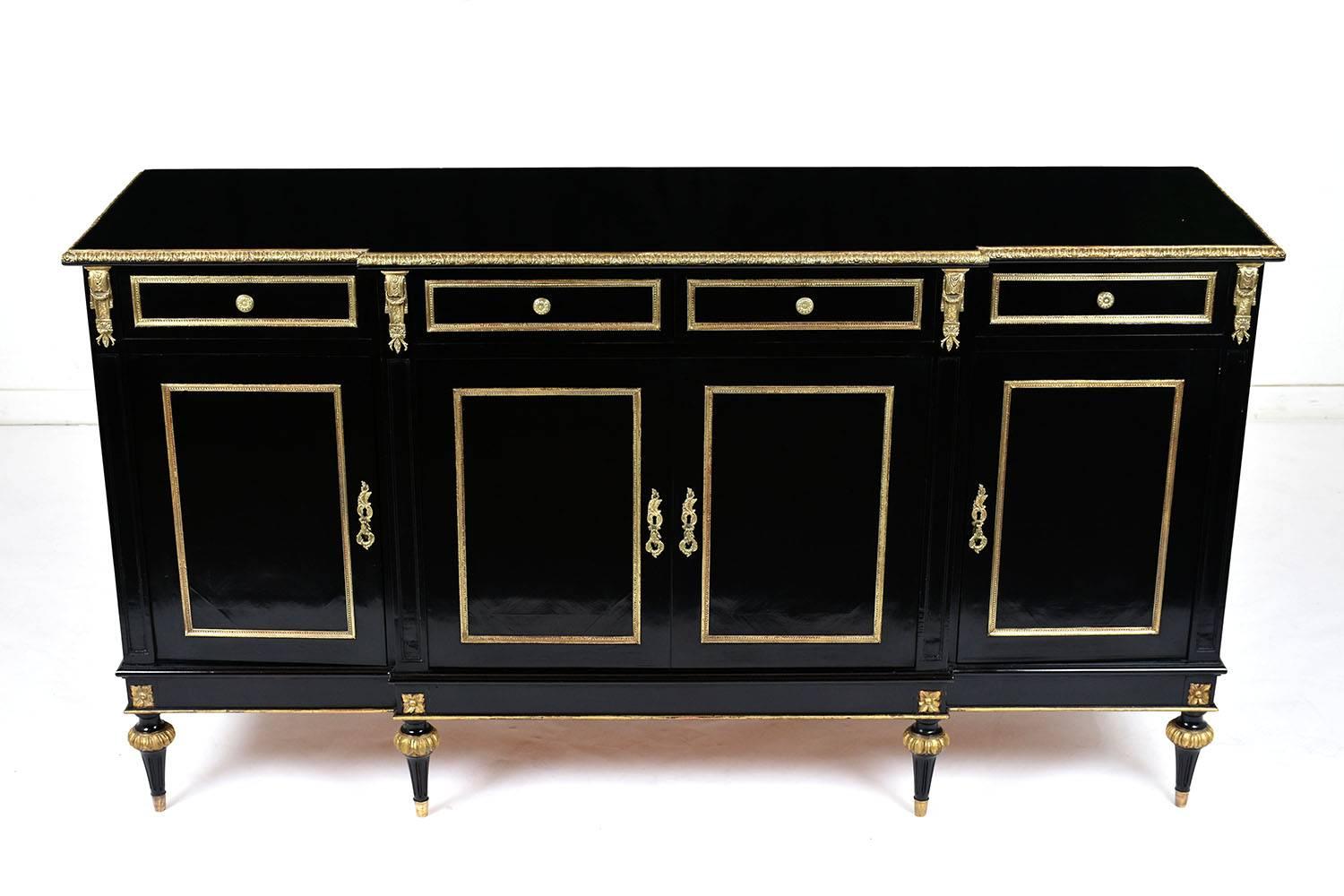 This 1970's Louis XVI-style buffet is made of mahogany wood ebonized a deep black color with a lacquered finish. The wood top features a beveled edge with brass moulding accents. There are four drawers with brass moulding accents and decorative