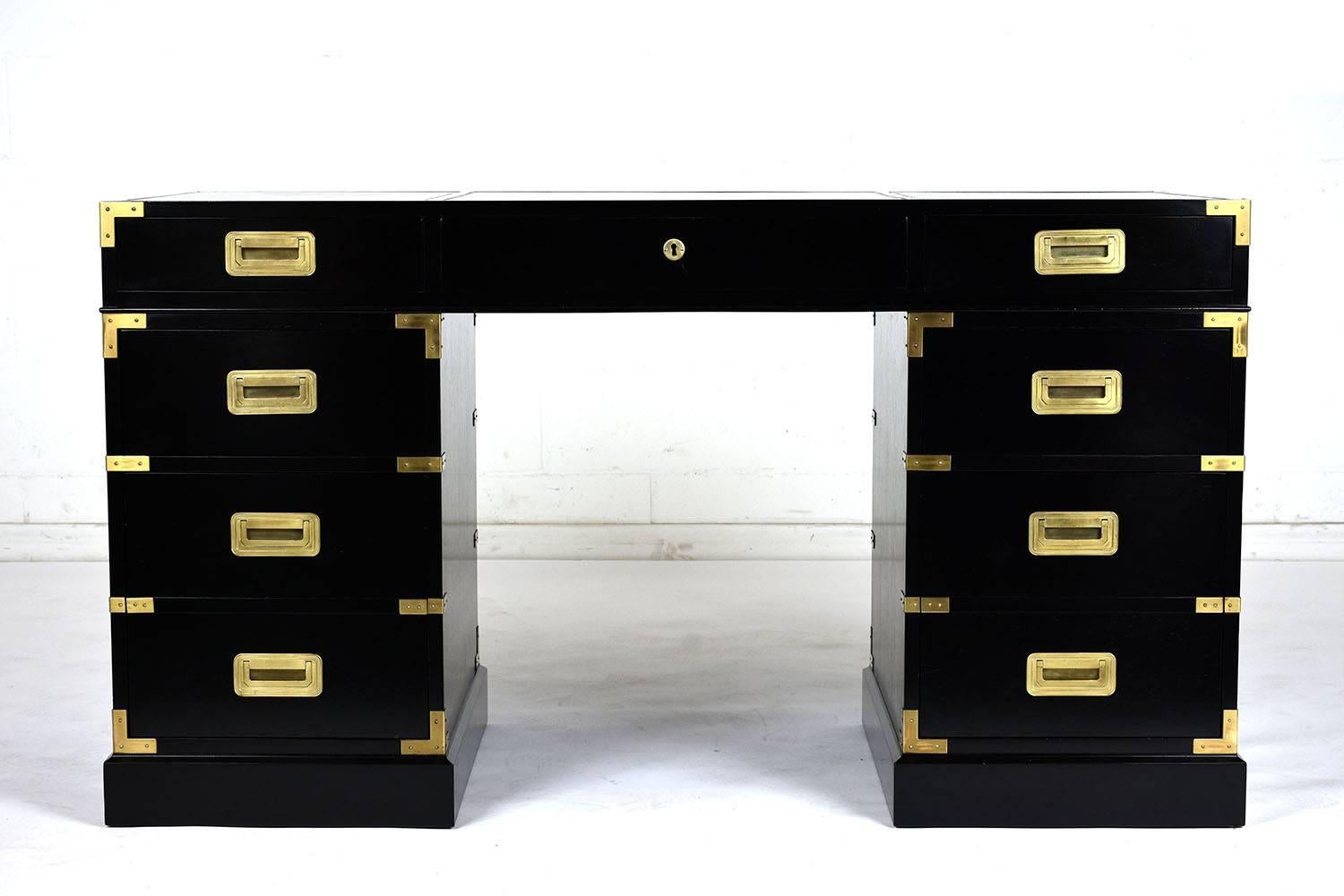 This 1960s Campaign-style mahogany desk has an ebonized and lacquered finish. There are seven drawers with the bottom two being double drawers for extra storage. The corners of the drawers and desk have brass accents and the drawers have brass