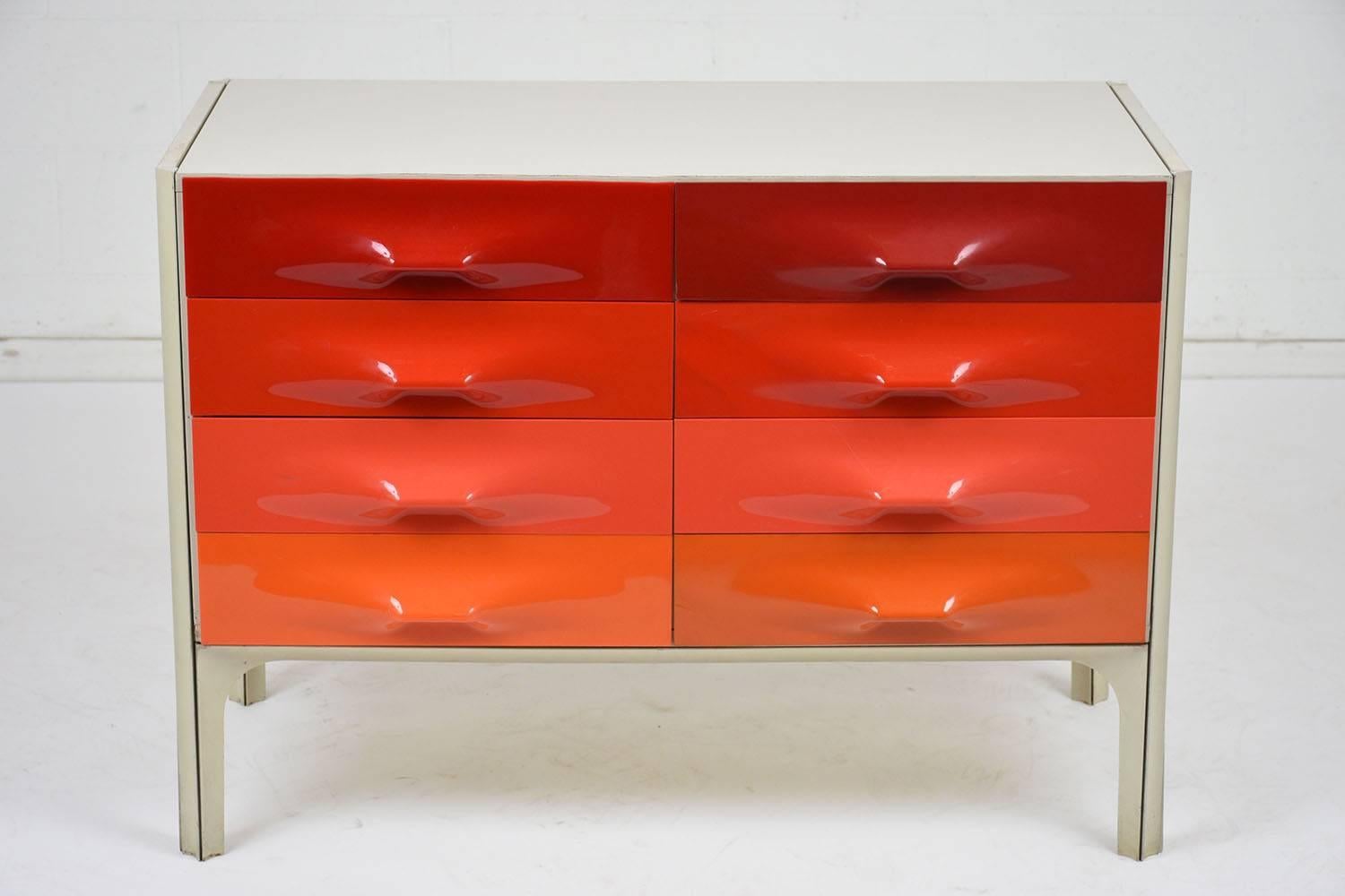 This 1960s Mid-Century Modern DF-2000 chest of drawers is designed by Raymond Loewy for Doubinsky-Freres. There are six drawers finished in varying tones of red and orange with plastic fronts and handles. The white laminate covered chest shows signs