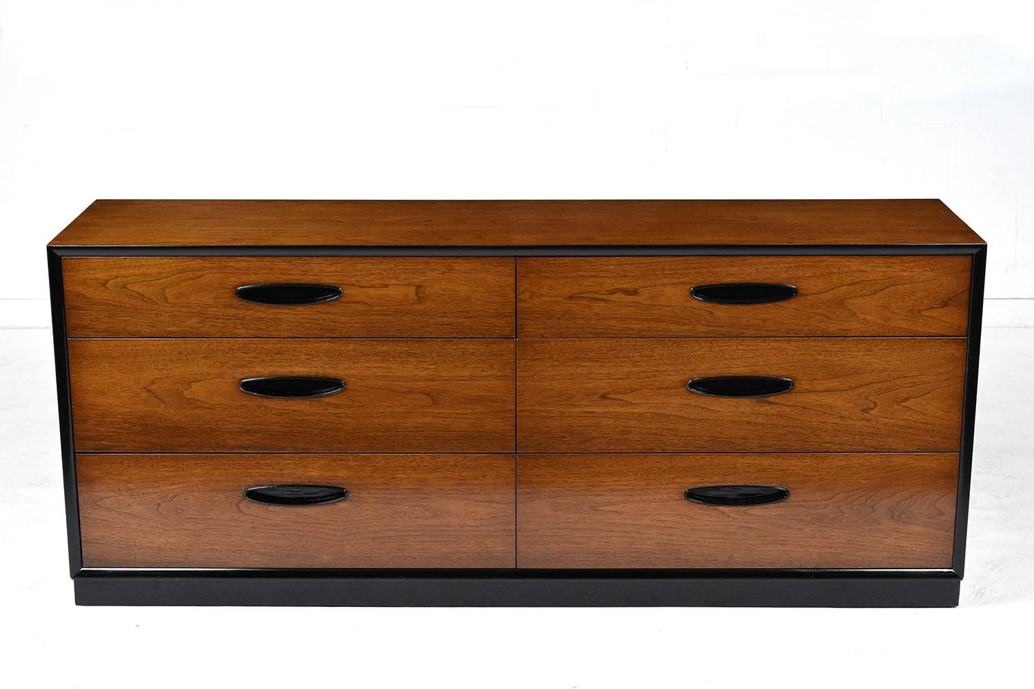 This 1960s Mid-Century Modern style chest of drawers is stained a rich walnut color with black accents and a lacquered finish. The six drawers have carved handles into the front stained in a black color. The chest has a pedestal base that is stained