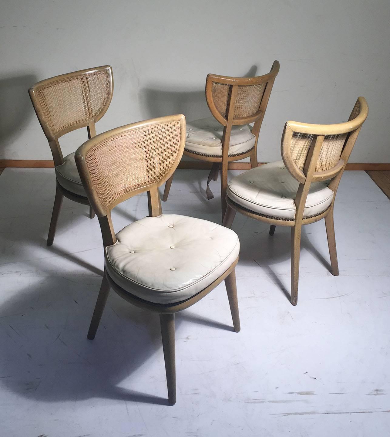 Vintage set of four American Mid-Century Modern chairs in the manner of William Haines, Paul Laszlo and Edward Wormley for Dunbar. 

These should be refurbished. The seats were done on white leather and may be of interest to preserve. Rattan is in