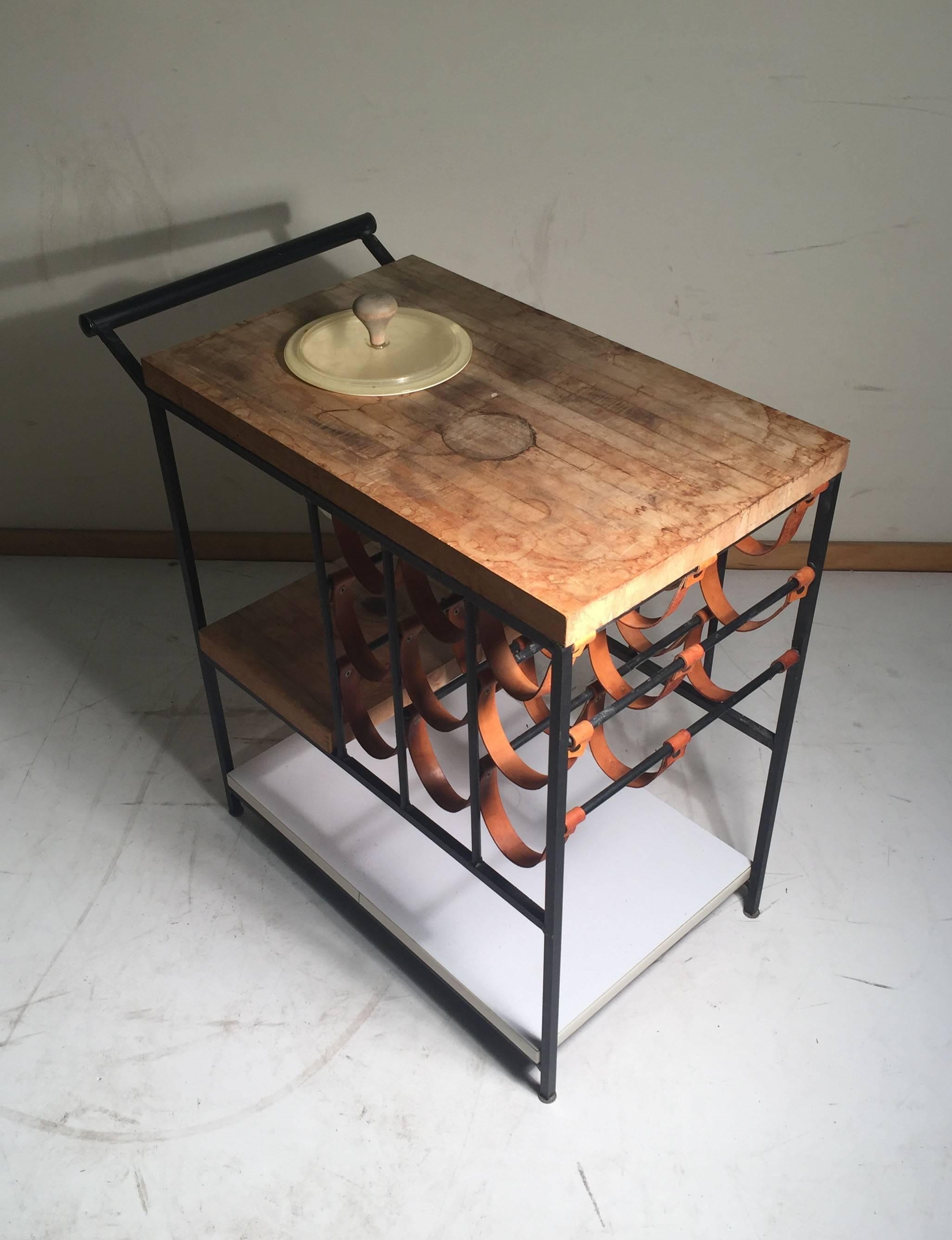 Beautiful example of Arthur Umanoff's bar cart with leather strap wine rack. 

Butcher blocks need to be sanded down. Cart includes the original castor wheels, but one of the castors is bent and needs to be restored if the intent is to use the