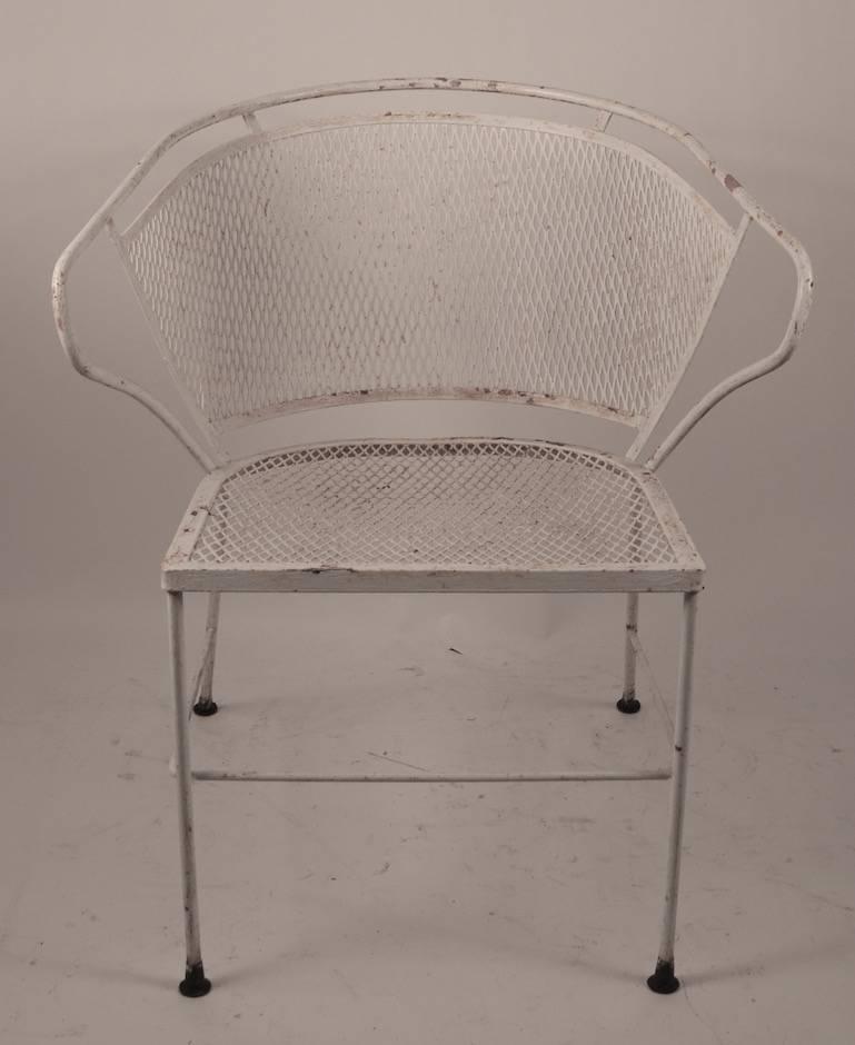 Nice pair of wrought iron and metal mesh outdoor patio, garden chairs, attributed to Woodard. Interesting wraparound back rest design, old white paint finish which shows wear normal and consistent with age. Some plastic glide feet have been