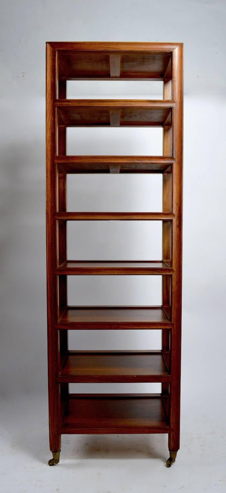 Interesting solid wood (mahogany) etagere comprising seven fixed shelves, on brass wheel coasters. This piece is marked 