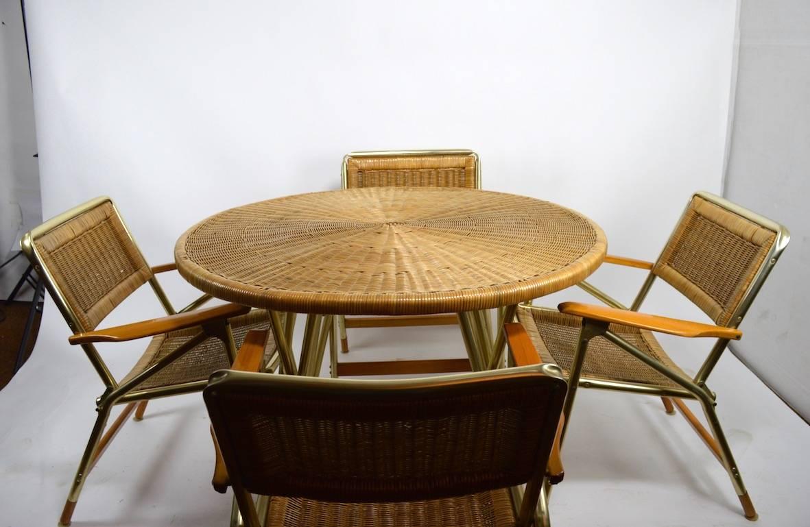 The set consists of four armchairs, and the circular table. Constructed of woven wicker, wood, and anodized aluminium, this set is in Fine original condition, clean and ready to use. All pieces fold down for storage and shipping. Comfortable,