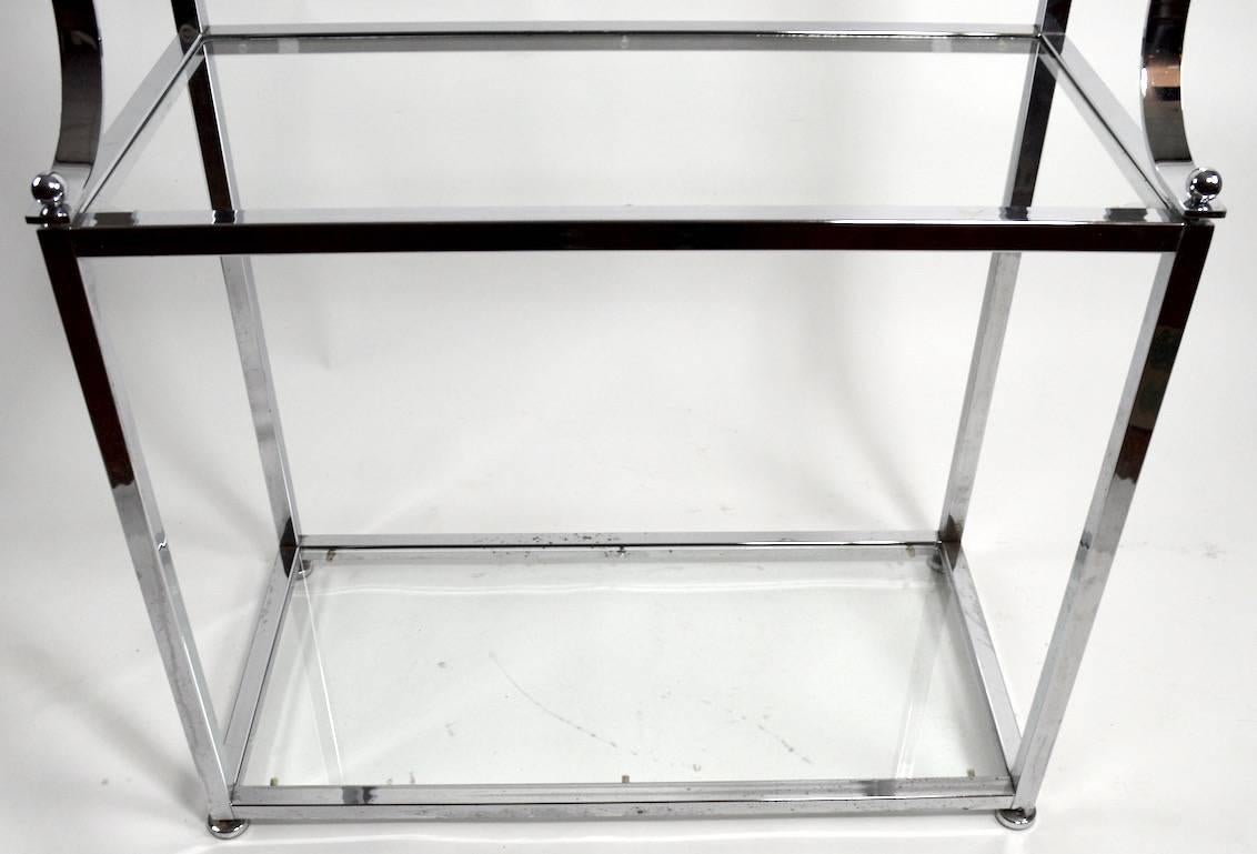 Chrome and glass vitrine in the Hollywood Regency style. This interesting étagère has a wider lower section with two large glass shelves (17.5