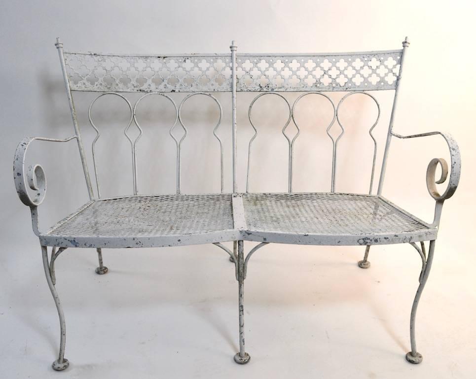 Nice two-seat wrought iron garden bench. Quatrefoil motif backrest, scroll form armrests and mesh seat. Paint finish shows wear, normal and consistent with age and use. Arm height 24