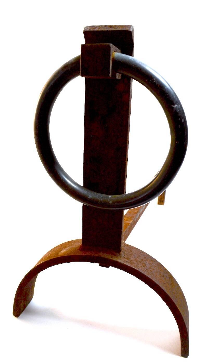 Modernist andirons design after Donald Deskey. Iron vertical support with large brass ring decorative element. These andirons are in original rust patina, and the brass ring has patinated, as shown.