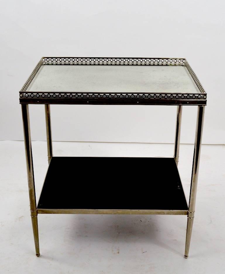 Plated side table with mirrored top, and black laminate lower shelf. The beveled mirrored top shows oxidation and wear, normal and consistent with age. Well constructed and chic side, occasional or lamp table, attributed to Maison Jensen.