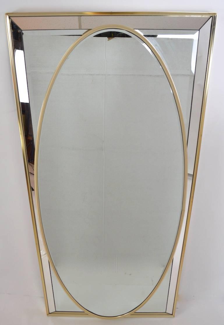 Interesting mirror on mirror construction, having an oval mirror placed on a rectangular mirror ground. Mirrors surrounded by brass tone anodized aluminium trim. Excellent original condition, clean, ready to install.