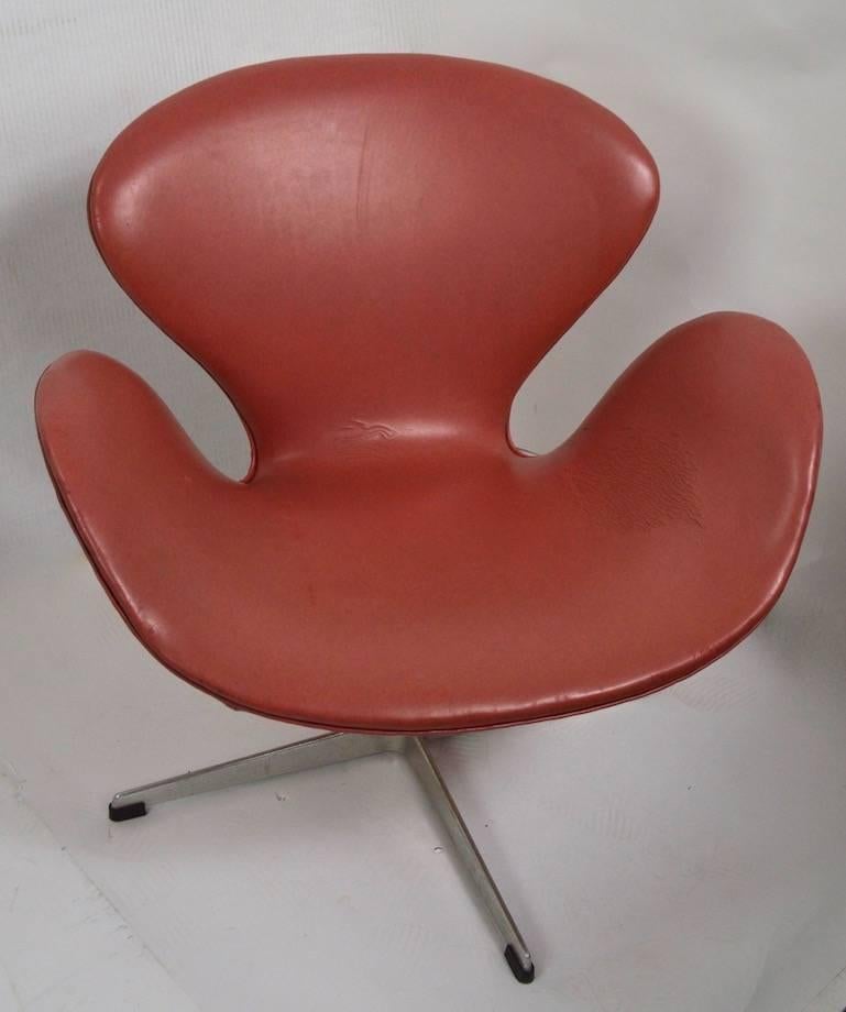 Swan chair designed by Arne Jacobsen for Fritz Hansen. This example is in its original Salmon color vinyl, which shows some wear, normal and consistent with age. The seat swivels on the cast aluminium base. Measures: Seat height 14, arm height 22