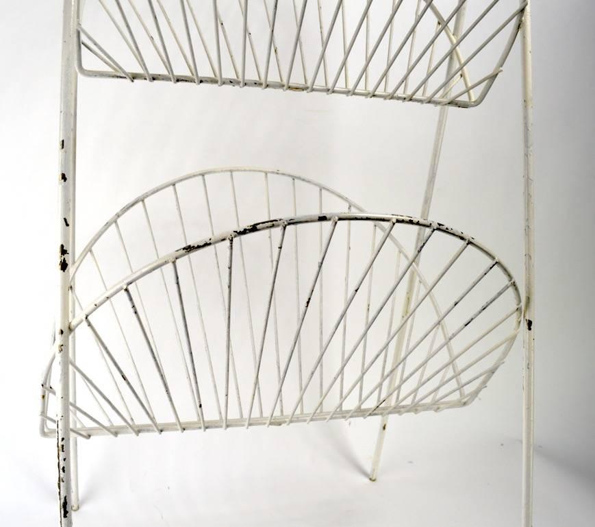 Stylish and dramatic iron and brass two-tier stand, functions as a magazine rack or catch all for a bathroom etc. The shelves are iron of semi circular form, the handle is faux bamboo, in solid cast brass. Shelves approximately 10 inches deep.