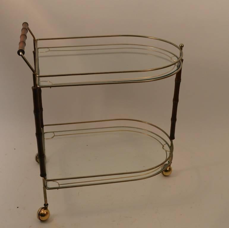 Two glass shelves, metal structure, with faux bamboo turned wood decorative elements. Serving cart rolls on original ball coaster feet. Height to top glass shelf 25"