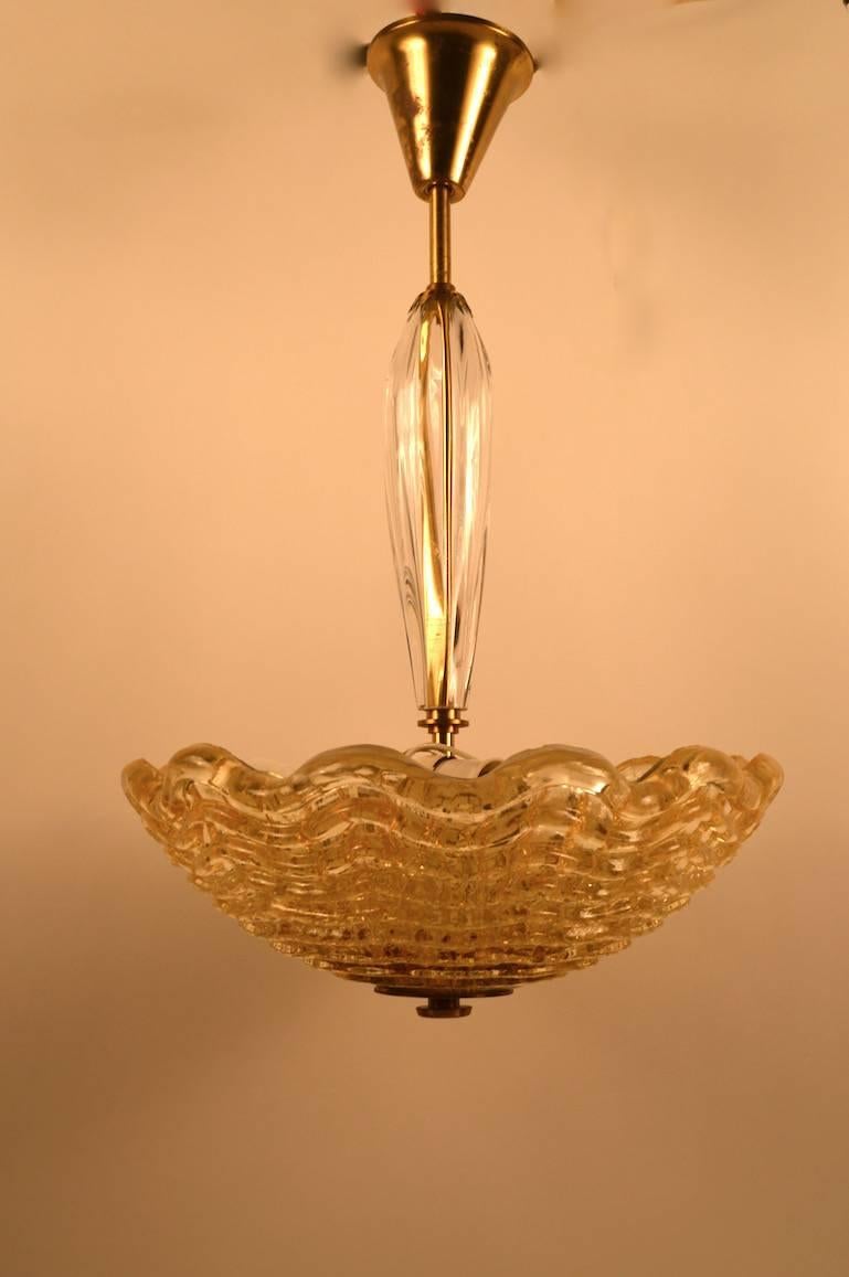 Glass bowl with wave pattern suspended from a clear glass stem, with three sockets set for standard US bulbs and installation.
This fixture creates a wonderful gold tone glow when illuminated.
Designed by Carl Fagerlund for Orrefors.