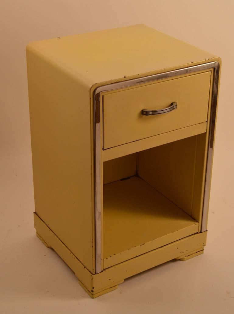 Nice Art Deco, Machine Age nightstand, designed by Norman Bel Geddes for Simmons Furniture Company. Pale yellow paint with bright chrome trim, and metal handle. This line of metal furniture was considered very Avant grade when first offered, and it