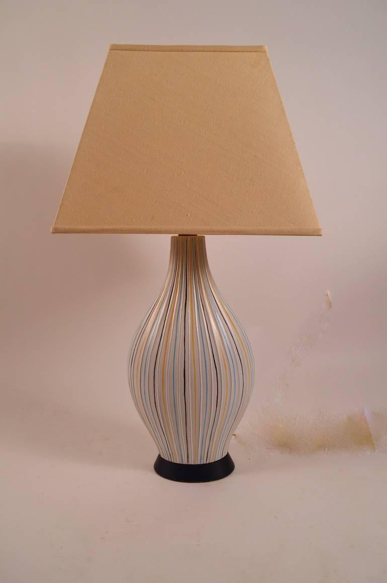 Lampe en poterie moderniste de forme ovoïde, peut-être italienne, vers les années 1950, montée sur une base en bois. Des bandes et des stries colorées courent verticalement sur le corps de la lampe. Récemment recâblé par un professionnel, état de