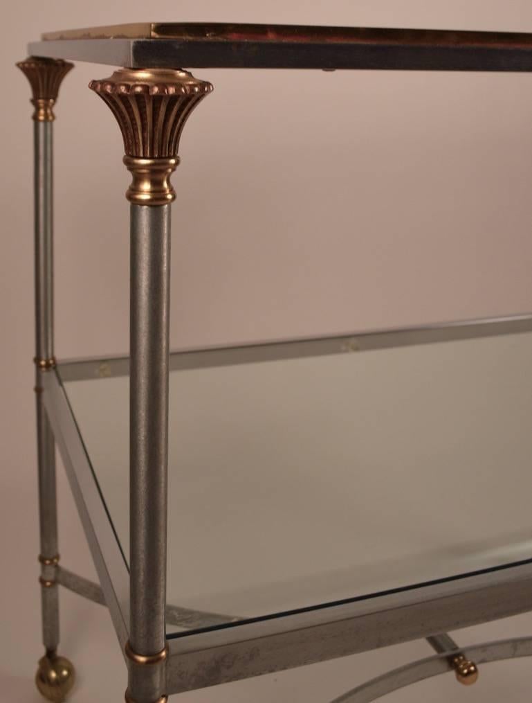    Brushed steel, brass, and glass serving,  bar cart attributed to Maison Jansen. 
This cart has two glass shelves, and is on original ball caster feet, allowing it to be moved to make serving easier.  
.