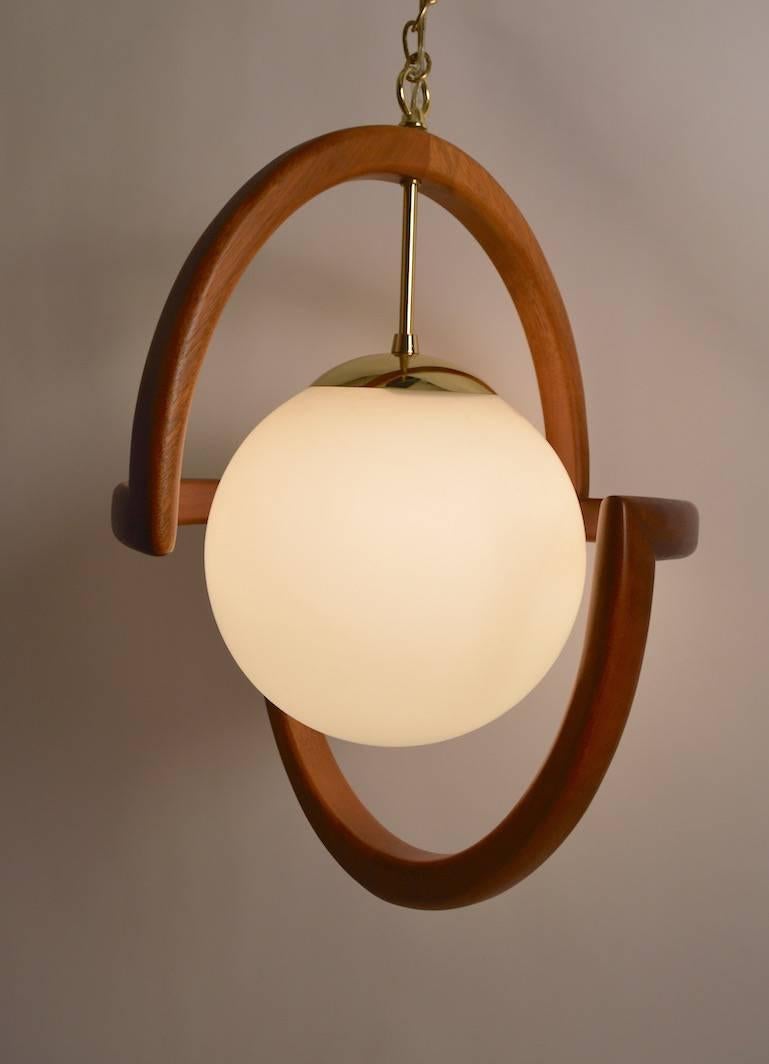 This fixture is Mid-Century American, in the Danish style. The frosted globe centre ball is surrounded by a continuous organic wood element. Currently the chandelier is set up as a swag light, with a long (140