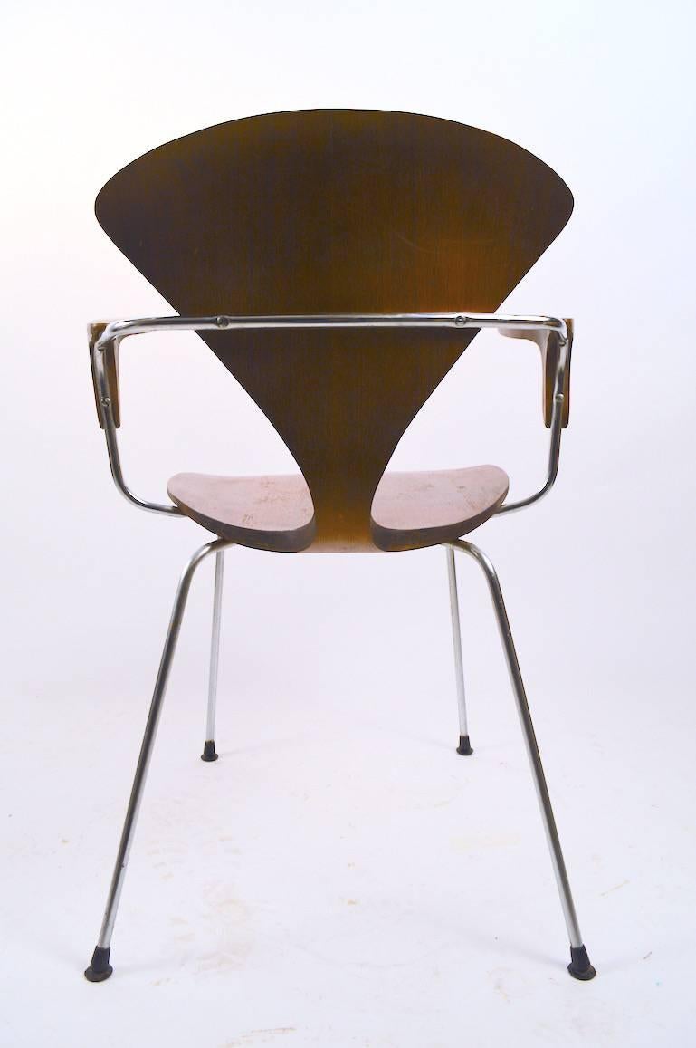 Dieser Stuhl hat eine durchgehende Rückenlehne und Sitzfläche aus gebogenem Sperrholz, Armlehnen aus Holzlaminat und ein verchromtes Rohrgestell. Die Holzoberfläche weist Abnutzungserscheinungen auf, und der Chromrahmen weist kosmetische Abnutzungen