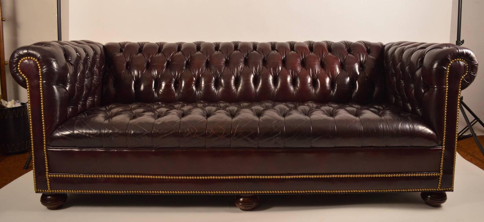 Classic tuxedo form, burgundy leather box sofa. Fully tufted, with decorative button studs. Very good original condition, ready to use. Measures: Seat depth 21
