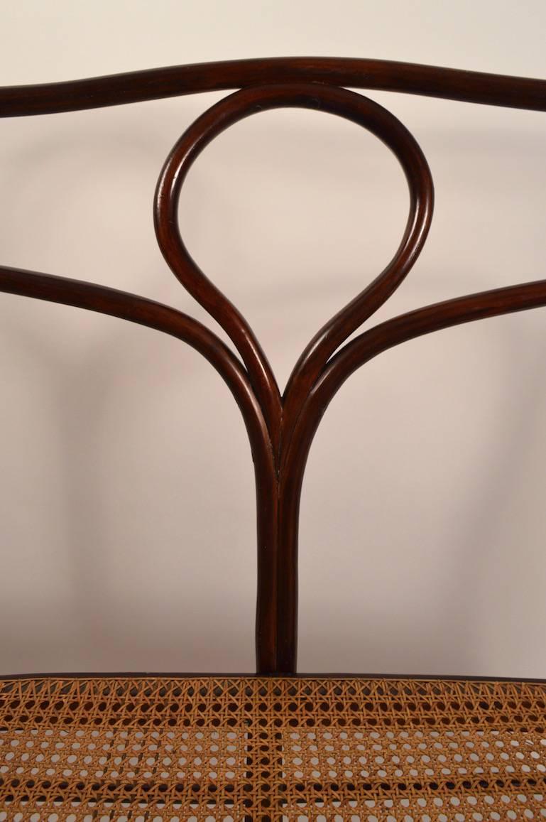 Secessionist bentwood bench, manufactured by J.J. Kohn, design attributed to Michael Thonet. Dark stain beech wood frame, with caned seat. Two extremely minor stress cracks in bentwood elements, normal and consistent with age. Marked 