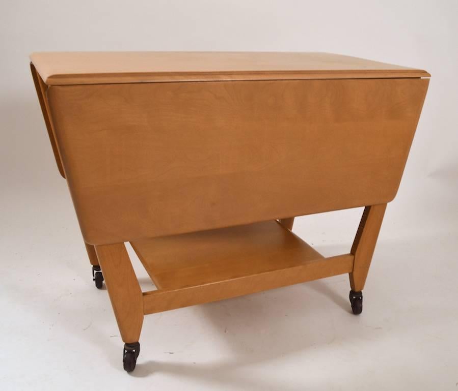 Rare item from the Classic Heywood-Wakefield modernist production period, this serving trolley cart was in production for only one year (1950-1952). The drop leaves each operate independently, allowing the cart to be used fully extended, closed, or