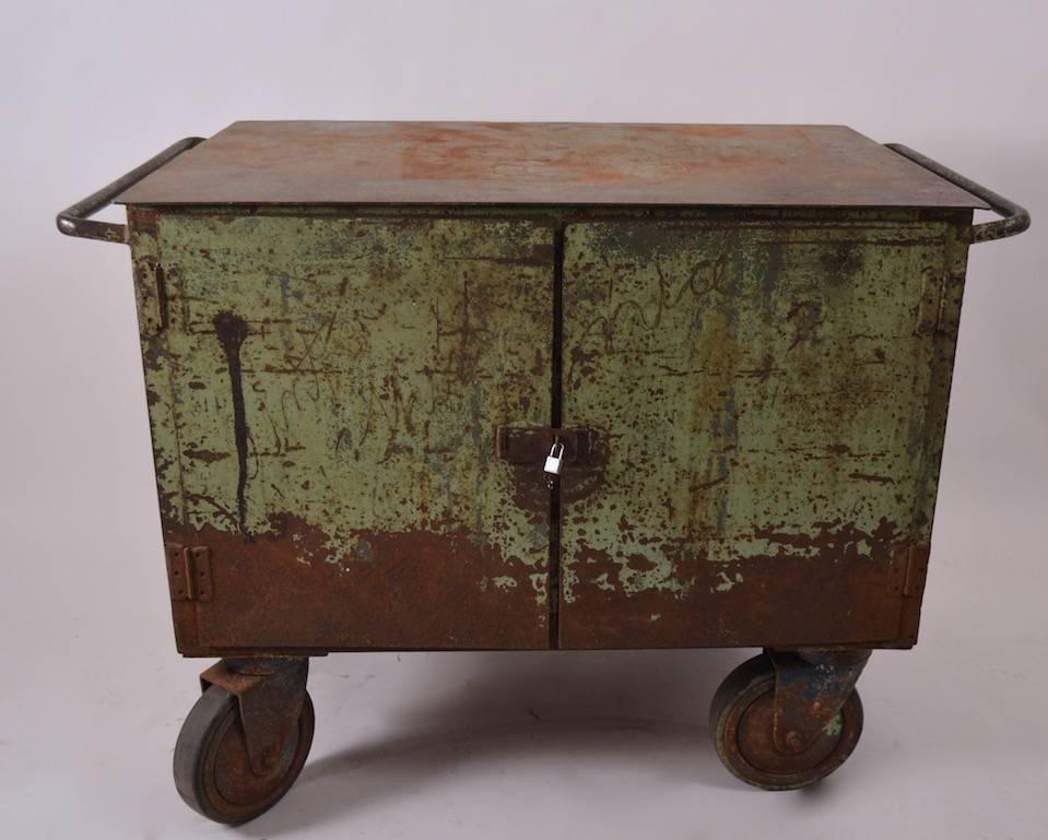 Two doors open to reveal three slide out drawers and an open storage compartment. The two front wheels pivot to allow the cart is moved around easily. Original finish, shows wear, normal and consistent with age, small lock included to keep doors
