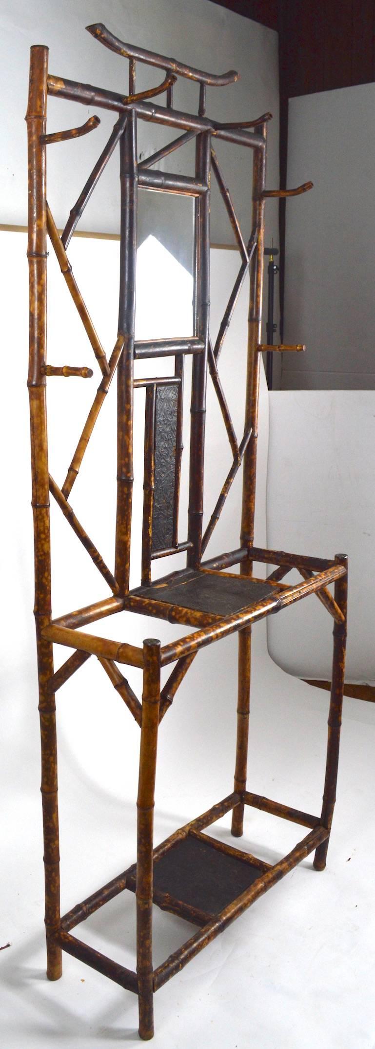 English Victorian bamboo hall rack, functions as a coat rack and umbrella, cane stand. The top center panel is a mirror, the other panels are embossed wood, the frame is bamboo. Height to shelf 34