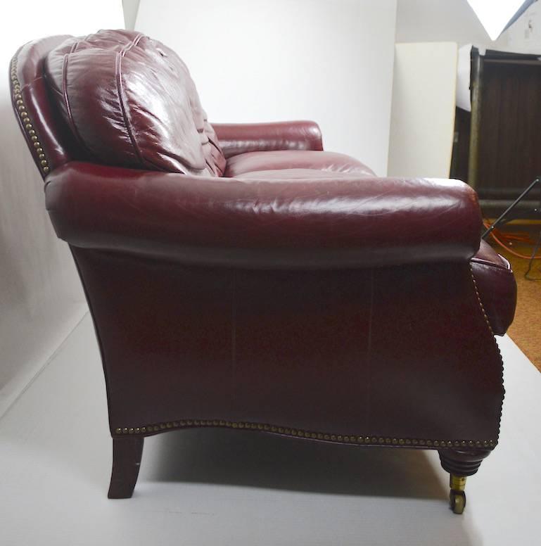 Comfy burgundy leather sofa, with brass studs. Classic form, original condition, clean, ready to use. Cushions do sit flat, they were just not placed correctly in the photo.
