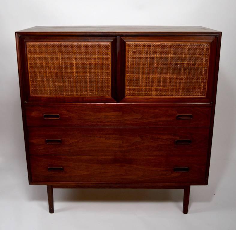 This cabinet has two doors which open to reveal divided storage space, over three deep drawers affording ample space for garments. 
 We believe this dresser is American made, in the Danish style. Walnut, and caned construction, very good original