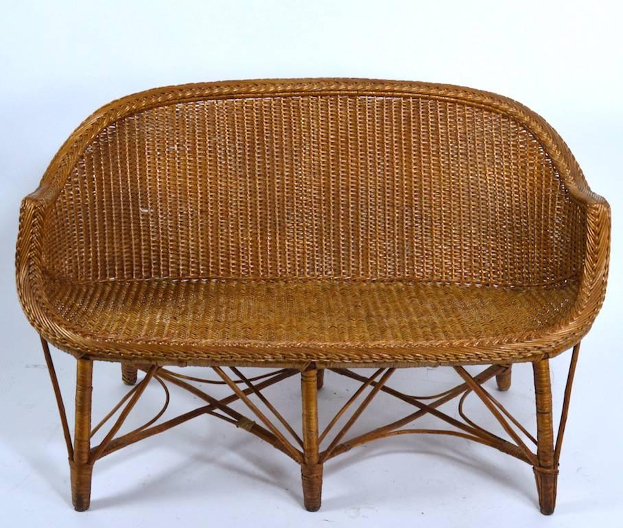 Woven wicker loveseat, settee in original condition. This example is in clean, ready to use condition; it does show some very minor loss to wicker, normal and consistent with age.
