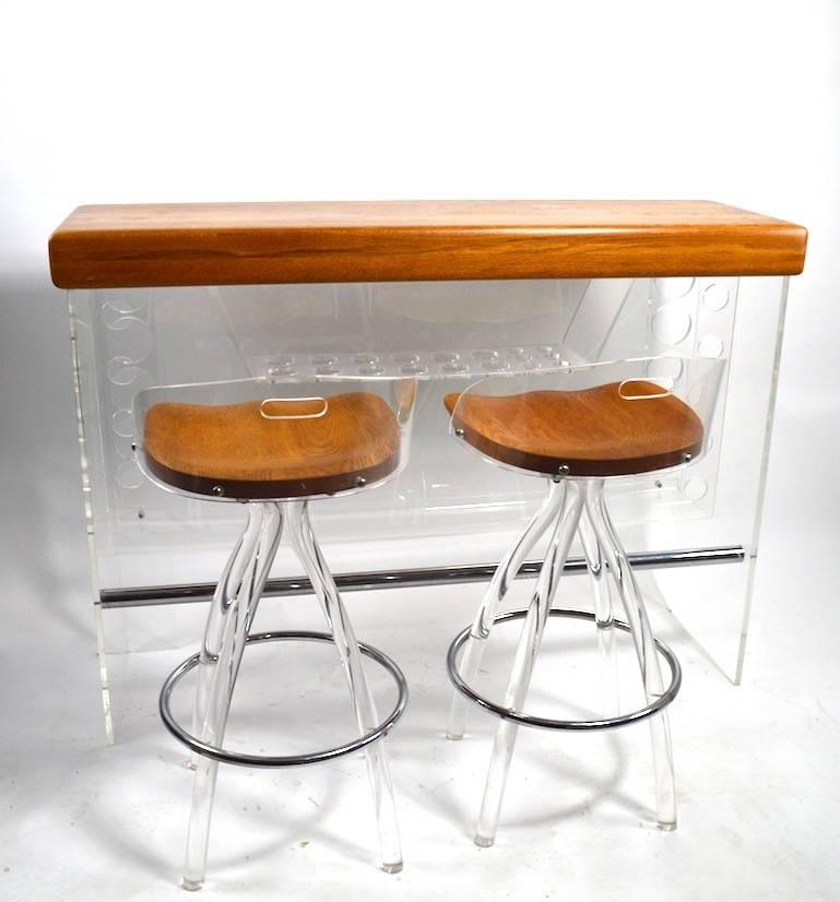 Very chic Lucite bar with oak top, comes with two Lucite and wood stools. The bar has a hidden light under the top surface, the stools swivel to adjust seating position. Dimensions in the listing are for the bar, stool dimensions as follows.