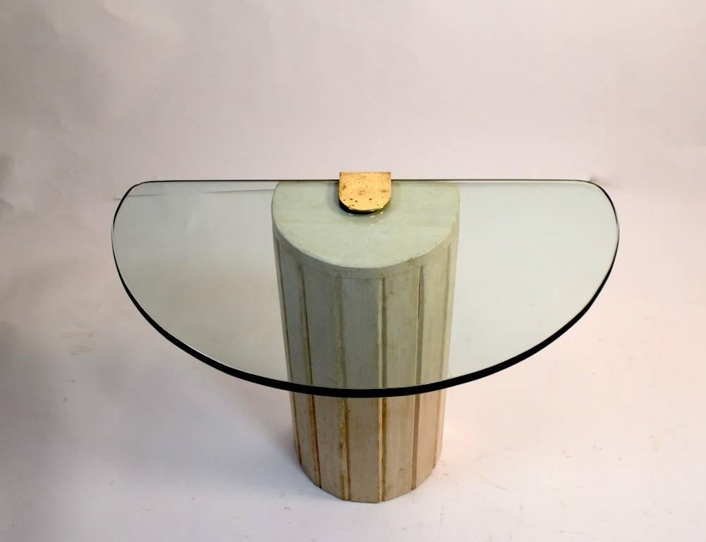 Diminutive glass top demilune end table with cast base. Off white columnar base, cast brass element holds thick semi circular plate glass top.