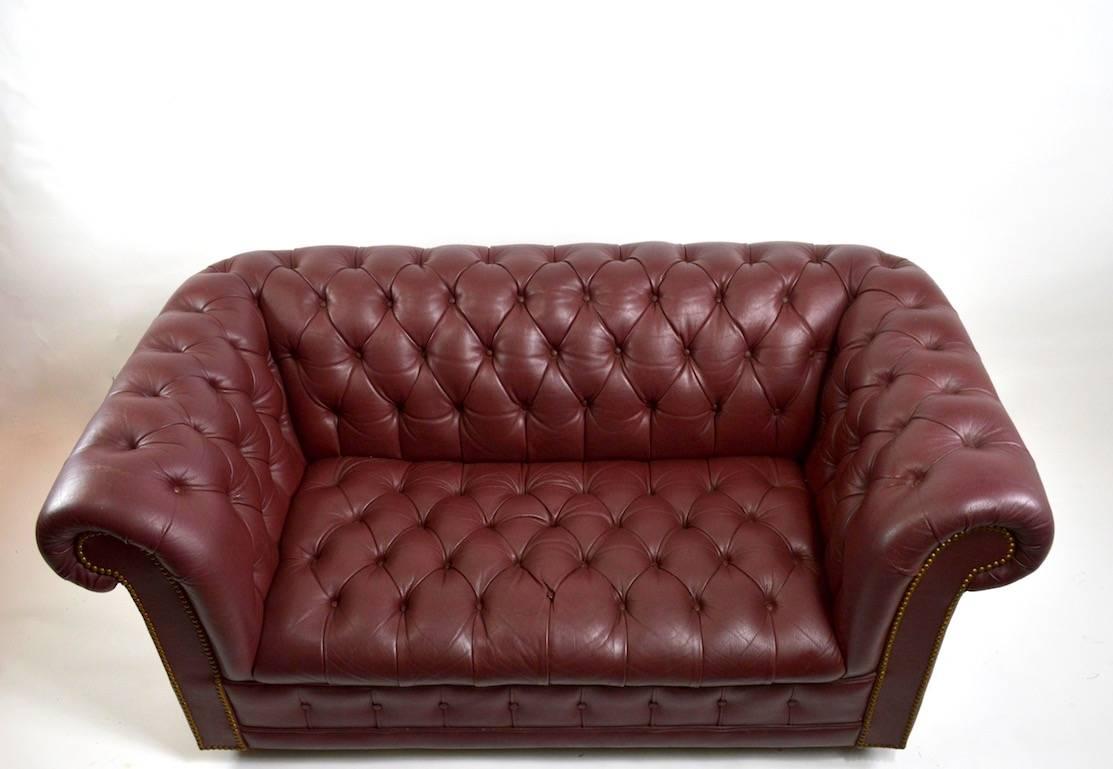 Nice loveseat size burgundy leather Chesterfield sofa. Very good vintage condition, shows some cosmetic wear, normal and consistent with age. Measures: Seat height 16.